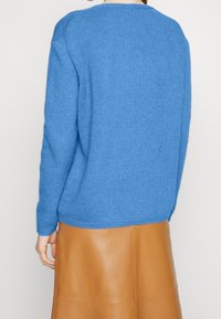 Maglione azzurro a maglia con collo rotondo, polsini e orlo a coste. Texture morbida abbinata a una gonna in pelle color cammello. Vista posteriore mostrata.