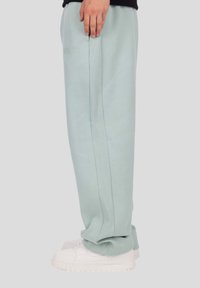 Világoszöld pamut melegítőnadrág bordázott oldalpanelekkel, gumis derékrésszel és szegélyekkel, fehér tornacipővel párosítva. Látható logók nélkül.