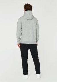 Sudadera gris con capucha ajustable, puños y dobladillo acanalados. Llevada con pantalones negros y zapatillas blancas, vista desde la parte posterior.