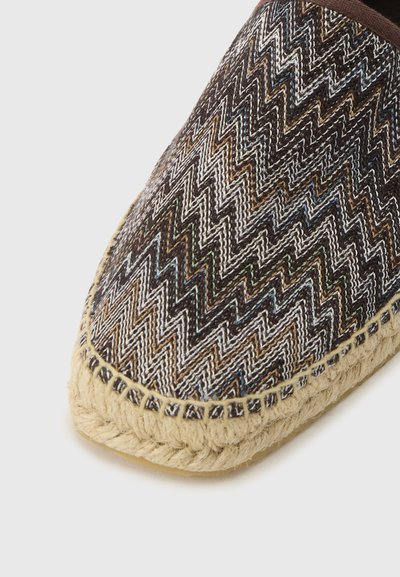 Gros plan d'une espadrille tissée avec une tige en tissu multicolore à motifs en zigzag et une semelle en jute naturel cousue.