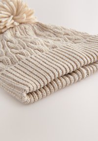 Gestrickte Mütze in Beige mit geripptem Bündchen und Zopfmuster. Mit rundem Bommel obenauf. Weiches, warmes Material.