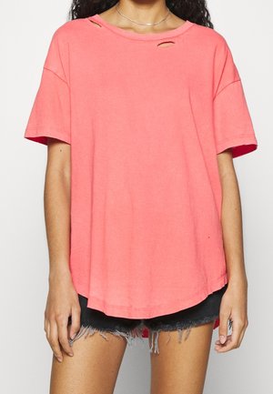 Korallowa, oversize koszulka wykonana z miękkiej bawełny z podwijanymi rękawami, z dwoma małymi wycięciami na ramieniu i zaokrąglonym dołem.