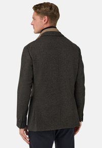 Ciemnoszary płaszcz z wełny o dopasowanym kroju i teksturowanej fakturze, z kołnierzem z wycięciem oraz mankietami na dwa guziki; cechuje się smukłą, strukturalną sylwetką.