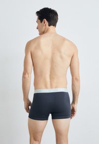 Férfi sötétszürke boxeralsó világosszürke derékkal, amelyen a Nike logó található, hátulról látható, sima tapintású és testhezálló fazonú.