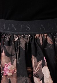 Blomstret nederdel med en sort elastisk talje med prægede bogstaver. Stoffet viser mørke blomsterprint i dæmpede nuancer.