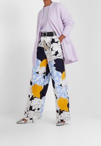 Liliowa kardigan, lekki sweter i szerokie kwiatowe spodnie w kolorze niebieskim, żółtym i czarnym, dopełnione srebrnymi szpilkami.