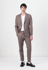 Kerged helepruun ülikond koos vastavate pükstega, ühekordne jakk, valge T-särk all, ja mustad slip-on kingad. Sujuv kangas ja terav lõige.