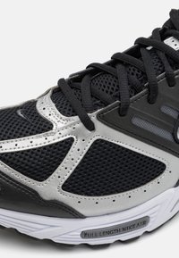 Čierna športová topánka so sieťovaním a syntetickými prekrytiami, s strieborným akcentom, textúrovanými šnúrkami a bielou podrážkou s detailom "FULL LENGTH NIKE AIR".