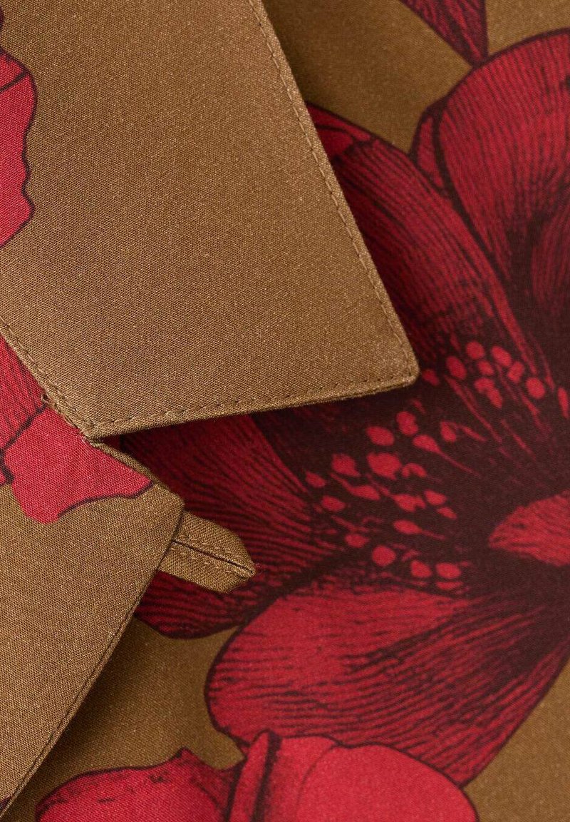 Tessuto con motivo floreale presenta fiori rossi su sfondo marrone. La texture appare liscia con dettagli di cucitura evidenti e accenti.