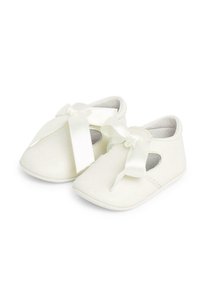 Weisse Stoffbabyschuhe mit einer abgerundeten Spitze, seitlichen Ausschnitten und einer großen Satin-Schleife auf jedem Schuh. Weicher, strukturierter Oberflächen.