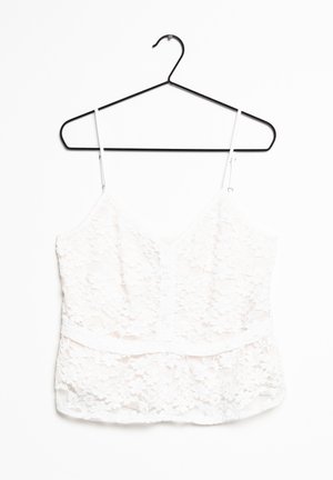Camisole blanche en dentelle avec des bretelles réglables, décolleté en V, motif floral et une finition douce et texturée, suspendue à un crochet noir.