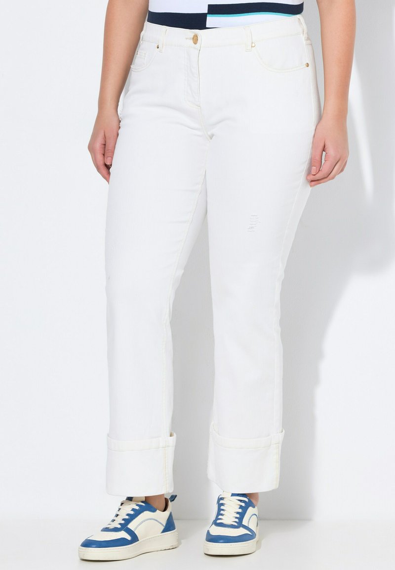 Vaqueros de mezclilla blanca con corte recto, puños enrollados y un ligero desgaste. Combinados con zapatillas azules y blancas. Presenta detalles en botones dorados.