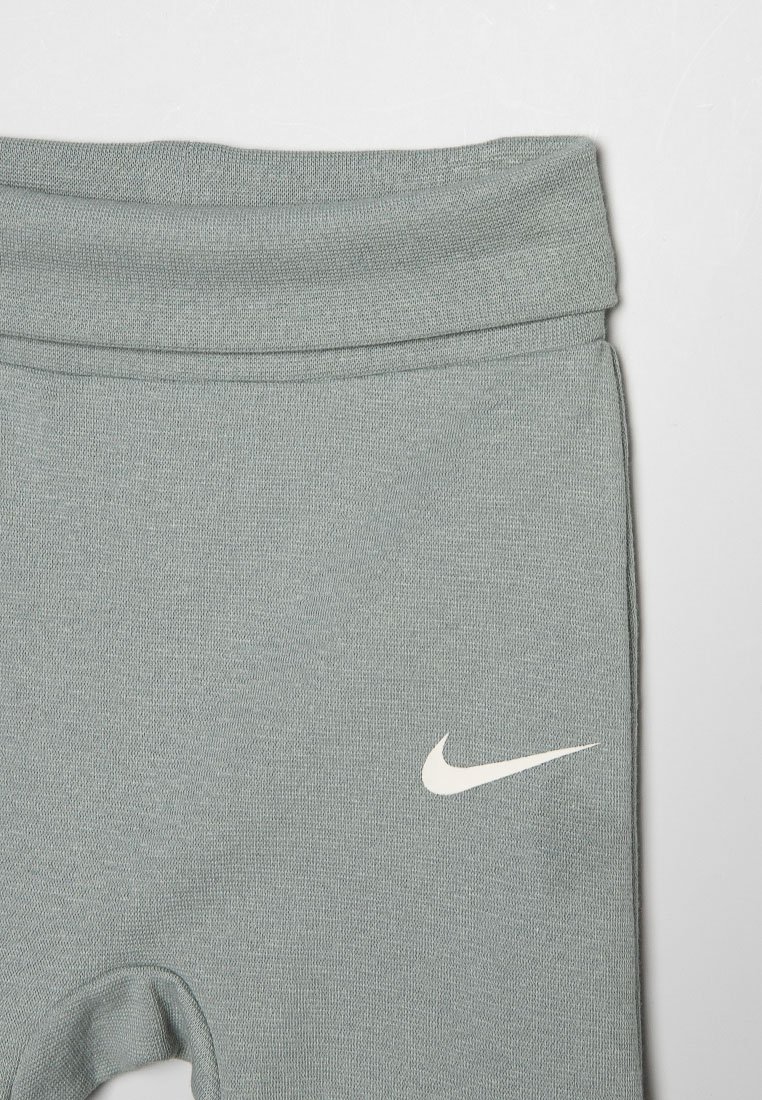 Leggings de sport gris clair en tissu doux et à la texture lisse, avec un logo Nike swoosh blanc près de la taille.