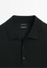 Schwarzes Merinowoll-Polohemd mit weicher Textur, Drei-Knopf-Leiste und klassischem Kragen. Markenetikett auf der Innenseite des Kragens sichtbar.