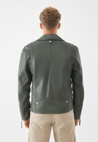 Mörkgrön läderjacka med snedskuren krage, dragkedjeförsedda ärmslut och detaljer i silver. Har en slät yta och en figurnära silhuett.