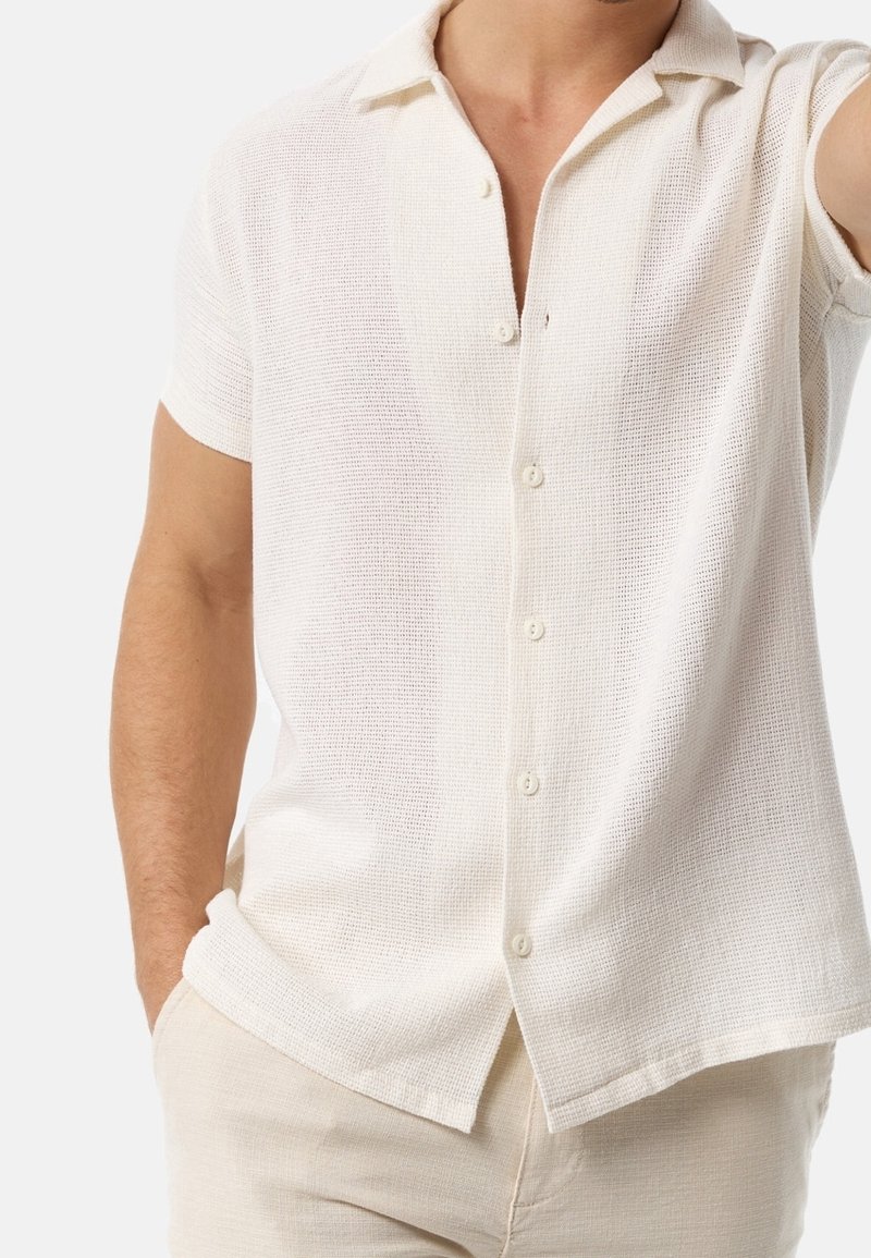 Short-sleeve white woven shirt with a collar, featuring a button front, textured fabric, and straight hem.
