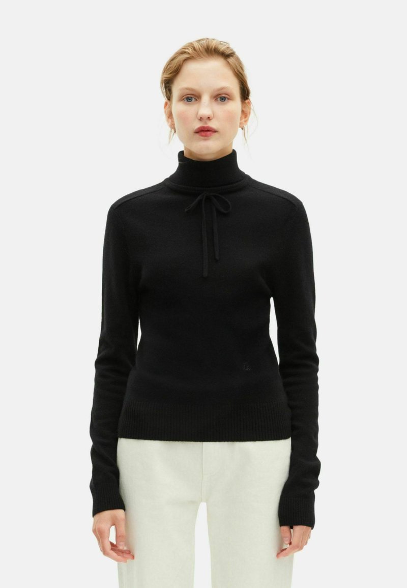 Jersey de cuello alto negro con una textura suave, presentando un detalle atado en el cuello, mangas largas y un dobladillo acanalado ajustado.