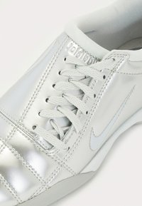 Zapatillas sintéticas plateadas con un acabado metálico brillante, que cuentan con un diseño de cordones, cuello acolchado y detalles acolchados.