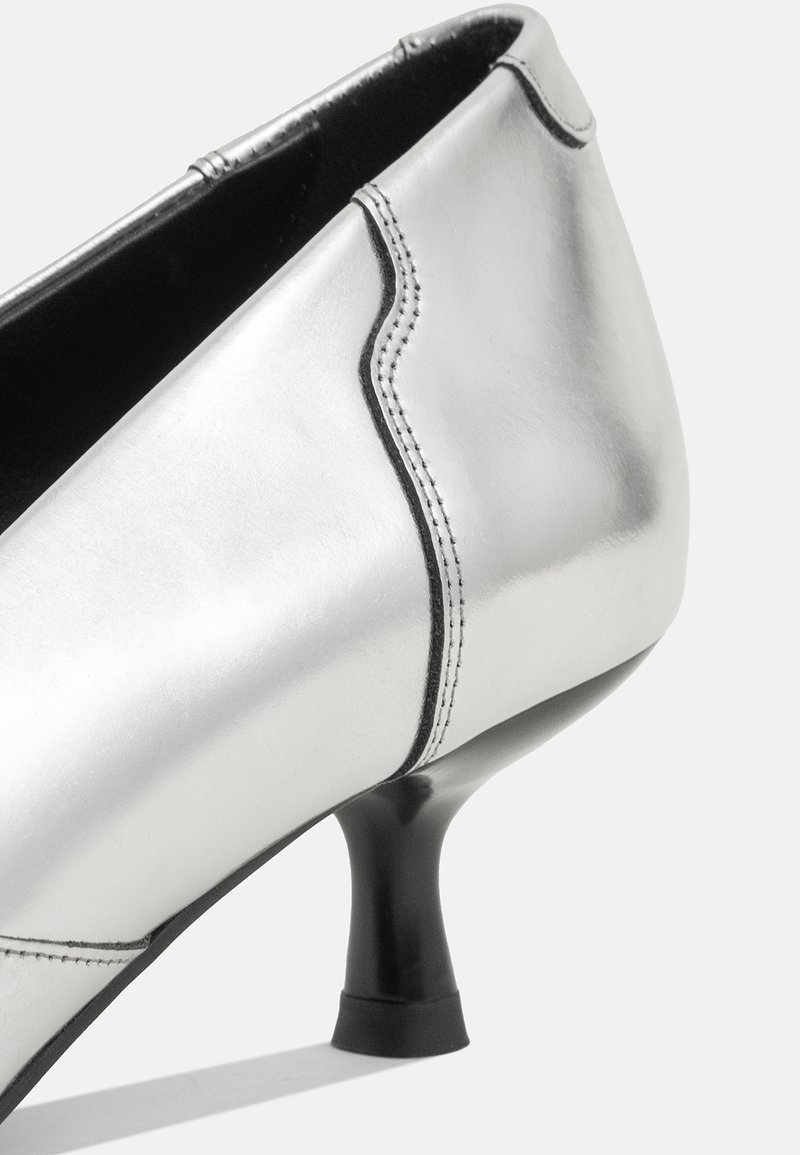 Scarpa con tacco alto in pelle argentata, con punta affusolata, cuciture nere e un tacco stretto e svasato. Texture liscia con una finitura elegante.