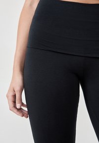 Mustat korkeat leggingsit, jotka on valmistettu joustavasta ja sileästä kankaasta. Ominaisuuksiin kuuluu leveä vyötärönauha ja istuvat lahkeet ilman näkyviä saumoja.