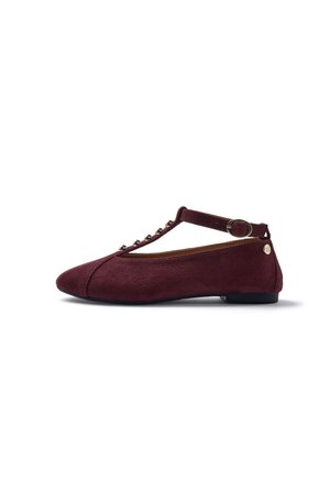 Zapato plano burdeos con tira en T, tachuelas redondas plateadas, cierre con hebilla y pequeño detalle de logo dorado en el talón.