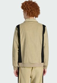 Beige corduroy jacket with black side panels, a classic collar, and ribbed cuffs, shown from the back with matching beige pants.