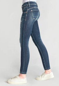 Jeans ajustados de mezclilla de color azul oscuro, con cintura alta y bolsillos traseros con herrajes de color cobre. Textura ligeramente desgastada.