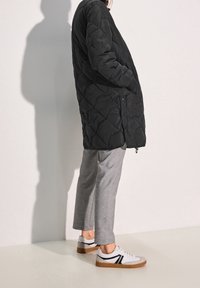 Svart vadderad lång kappa med sidofickor, ihop med ljusgrå avsmalnande byxor och vita sneakers med svarta detaljer och sula i gum.