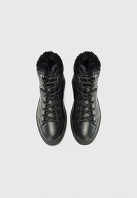 Bottes montant noires avec doublure en fourrure, dotées d'œillets en métal et de lacets, présentées de haut en bas sur un fond uni.