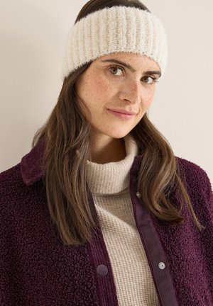 Gebreide crèmekleurige oorwarmer met geribbelde structuur; gedragen bij een gebreide beige trui en een donkerpaarse jas met een corduroy kraag.