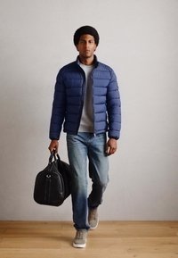 Doudoune bleu marine, t-shirt gris, jean bleu clair, baskets grises et sac de sport noir. Texture lisse avec un motif matelassé.