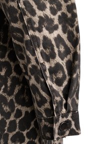 Tela de estampado de leopardo en tonos marrón y negro con textura de denim, que presenta un puño abotonado y detalles de costura visibles.