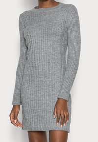 Abito a coste grigio a maglia con maniche lunghe, dotato di scollatura rotonda e motivo testurizzato. Lunghezza a metà coscia con silhouette aderente.