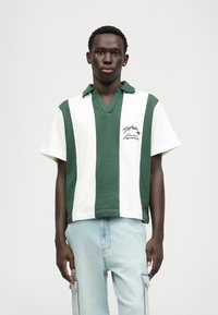 Groen en wit gestreepte korte mouwen polo met een v-hals, met een geborduurd tekstdetail aan de linkerkant.