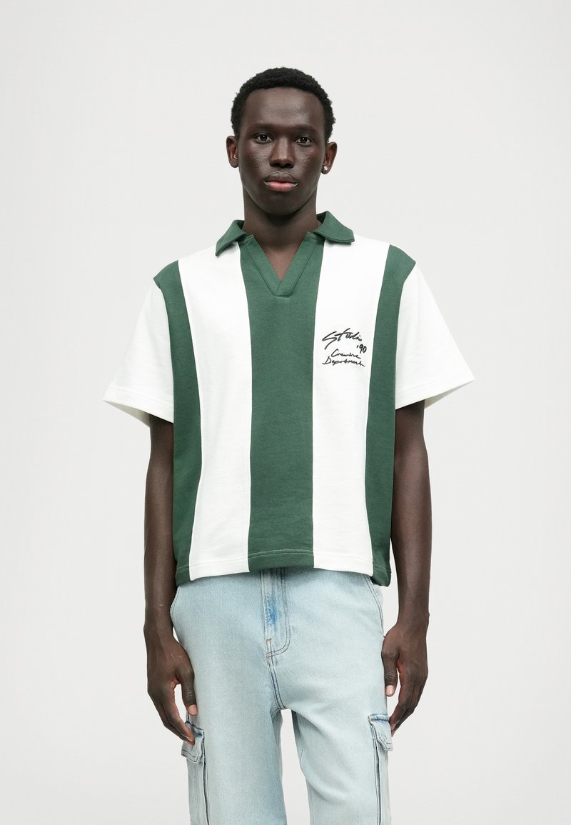Polo vert et blanc à rayures, à manches courtes et col en V, avec un détail de texte brodé sur le côté gauche.