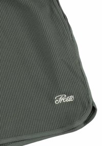 Ciemnozielony, żebrowany materiał z falistym brzegiem, z białym haftowanym napisem marki "Prosto" blisko dolnego rogu.