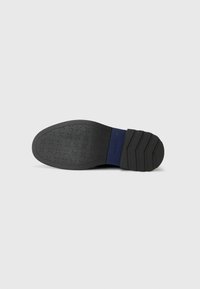 Suela de zapato de goma negra con un patrón texturizado y un acento azul en el talón. Presenta un diseño plano y cónico con ranuras horizontales.