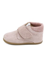 Zapato de bebé de ante rosa suave con una amplia tira de velcro, puño acanalado en el tobillo y suela de goma marrón, mostrado de lado sobre un fondo blanco.