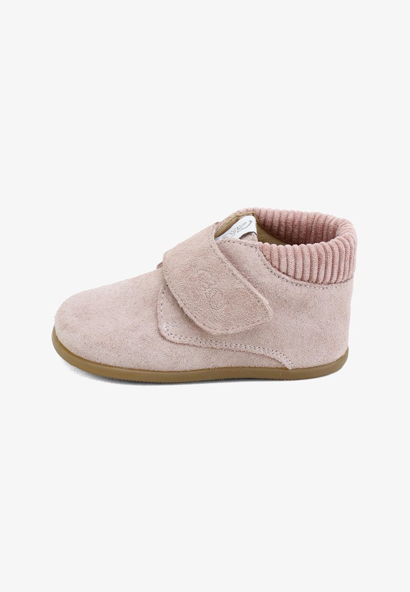 Zapato de bebé de ante rosa suave con una amplia tira de velcro, puño acanalado en el tobillo y suela de goma marrón, mostrado de lado sobre un fondo blanco.