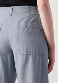 Light gray pants with a smooth, textured fabric. Features two large back pockets, stitched detailing, and a mid-rise waistband.