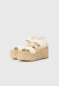 Sandales compensées blanches avec une semelle en espadrille tressée, dotées de larges brides et d'une boucle de cheville réglable. Texture lisse avec une semelle intérieure beige clair.