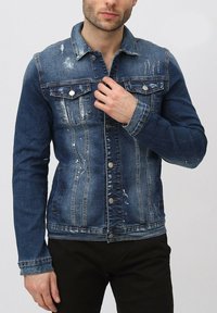 Veste en denim bleu foncé avec des zones décolorées, deux poches poitrine et des boutons métalliques. Comprend un col classique et des manches longues.