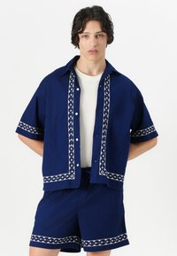 Navy blue short-sleeve shirt with white embroidered patterns along the collar and sleeves, paired with matching shorts featuring similar detailing.