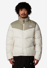 Vadderad jacka i krämfärg och ljusgrön med hög krage, framzipper och sidofickor. Har logotyp på bröstet och en karaktäristisk chevron-design.