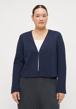 Navy cropped jacket with a deep V-neck and long sleeves, made from smooth fabric. Model wears a white top underneath.