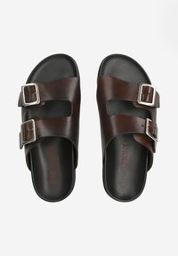 Sandales glissantes en cuir marron avec deux boucles argentées réglables, revêtement texturé et semelle intérieure noire et rembourrée. Nom de la marque visible à l'intérieur.