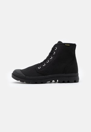 Schwarze Stiefeletten mit Obermaterial aus Canvas, Gummi-Zehenkappe und strukturiertem Sohlenprofil mit tiefen Profilrillen. Metallösen für die Schnürsenkel an der Seite.