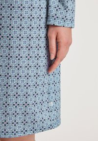 Tessuto blu con un intricato motivo floreale, caratterizzato da accenti blu navy e rosa. Il design copre il vestito, estendendosi fino a un orlo arrotondato.