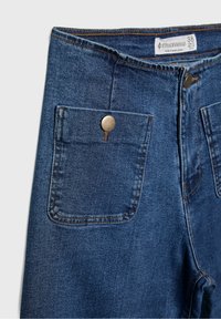 Modré džíny s vysokým pasem, přední kapsy s klopou zabezpečené kovovými knoflíky a viditelný označení značky na vnitřní straně pasu.