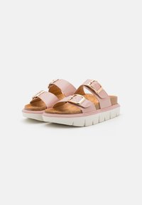 Sandales à glissière en vernis rose avec deux brides réglables, boucles dorées, semelle en liège et une semelle épaisse blanche. Texture lisse et design ouvert.